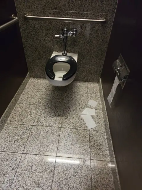 Restroom stall in an Indianapolis commercial facility before cleaning: paper debris on the stall floor
