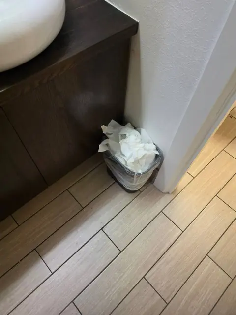 Restroom trash area in an Indianapolis commercial facility before cleaning: overflowing trash and debris beside a vanity